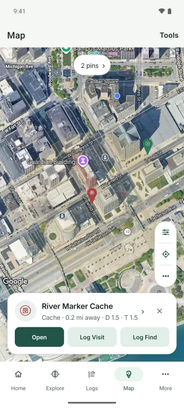 The map on Android with cache and adventure pins in downtown Detroit and River Marker Cache selected, with Open, Log Visit, and Log Find
